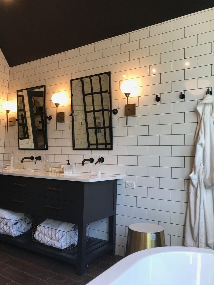 Modern bathroom with black vanity, white subway tile, two mirrors, and a white robe.