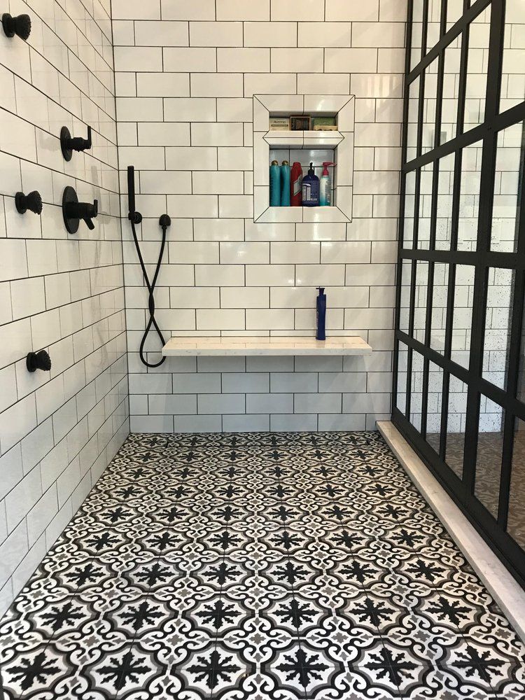 Shower with white subway tile walls, patterned black and white floor tiles, glass enclosure with black grid.
