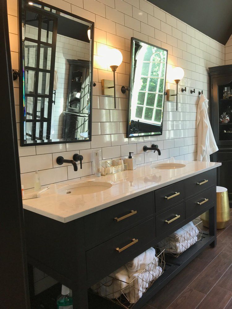 Bathroom with black vanity, white countertop, two sinks, mirrors, and sconces. White tile wall.