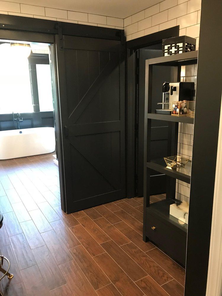 Black barn door and shelving unit in a modern bathroom with brown wood-look flooring.