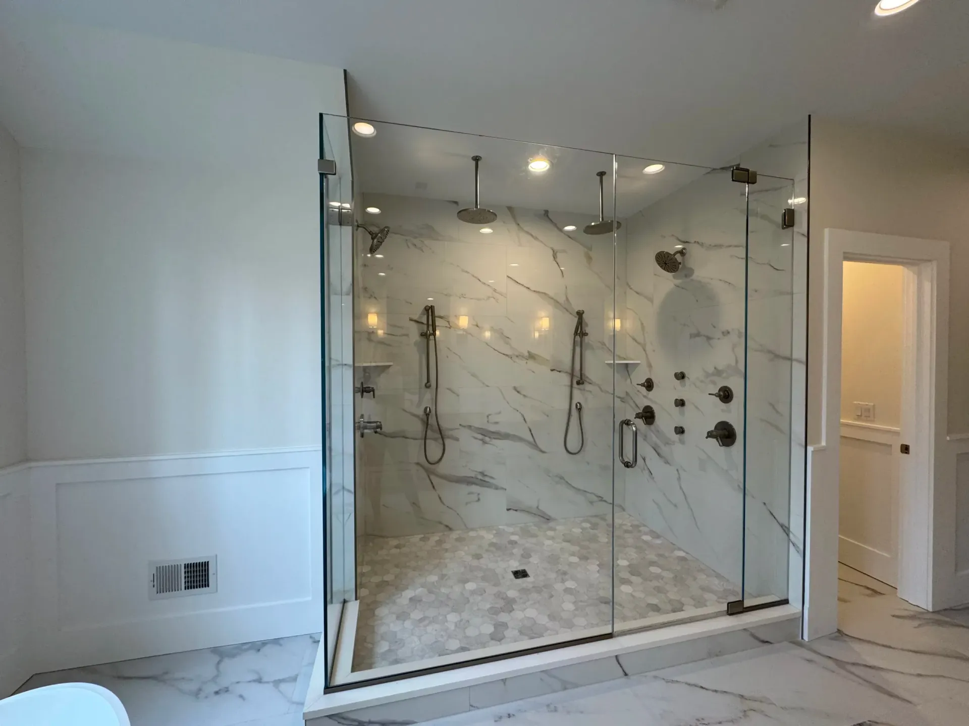 Large glass shower with marble walls and multiple showerheads; a luxurious bathroom.