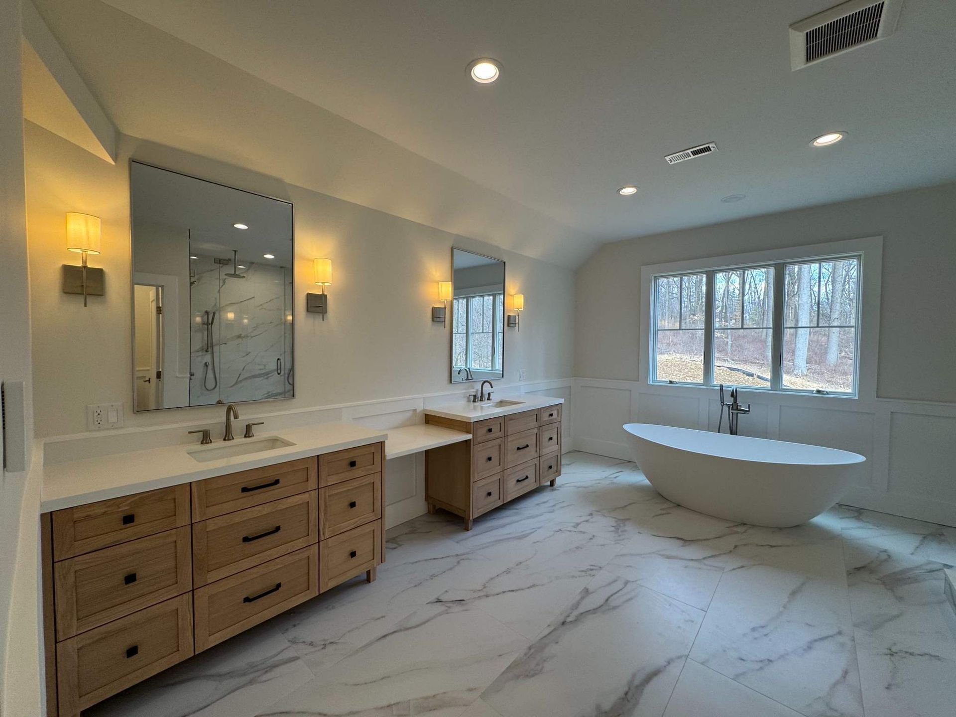 Spacious modern bathroom with marble floor, wooden vanities, soaking tub, and large mirrors.