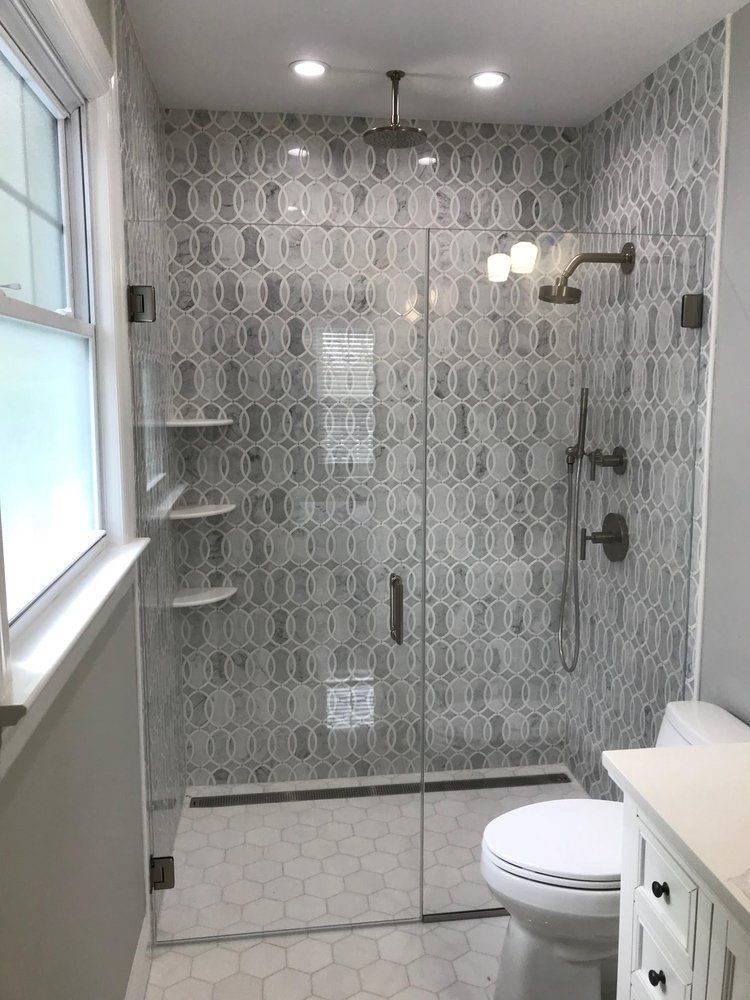 Shower with patterned gray and white tile, glass door, shelves, and toilet.