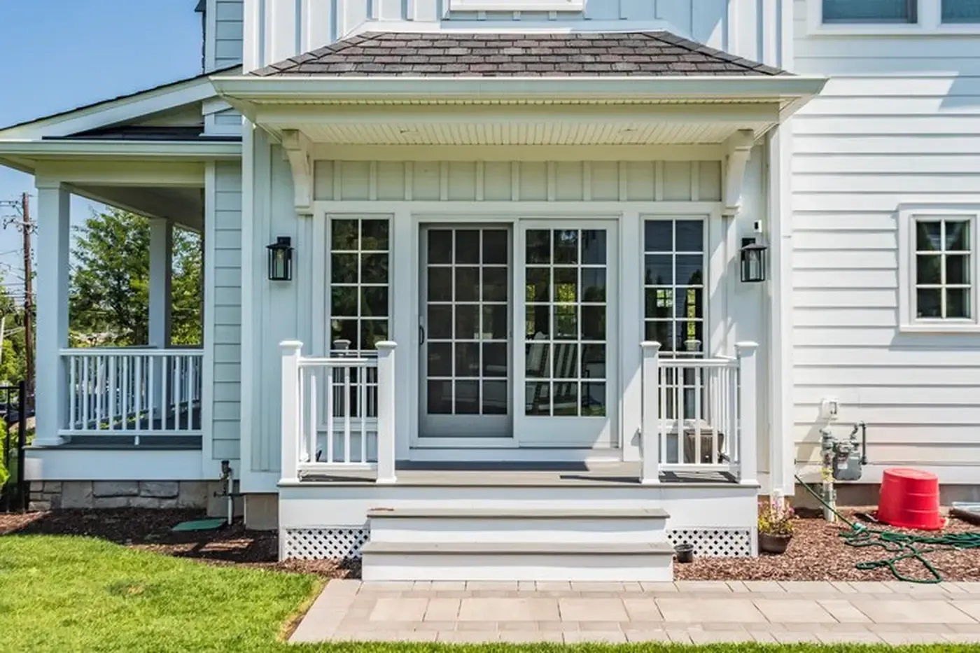 White house with porch, steps, and glass doors. Gray roof, white trim. Green grass and stone walkway.