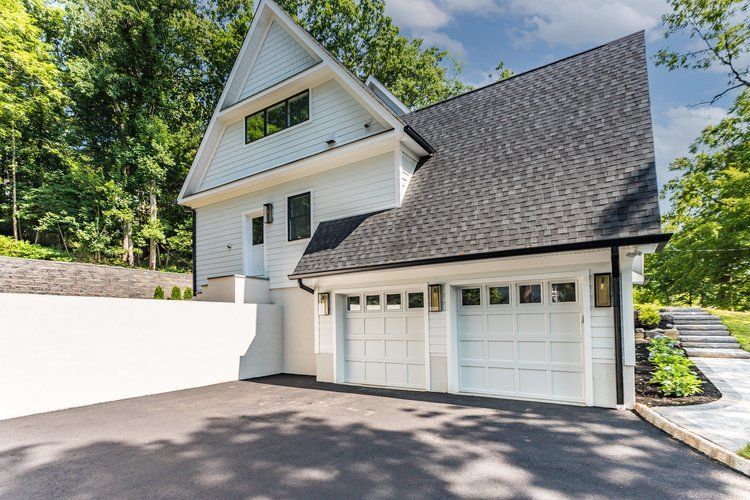 White house with black roof and garage doors, black asphalt driveway.