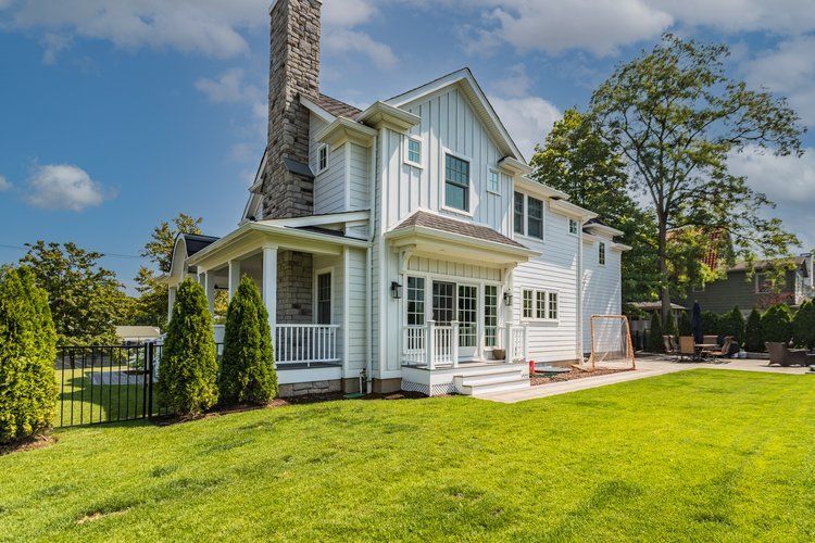 White house with porch, chimney, and large backyard with green grass under a blue sky.