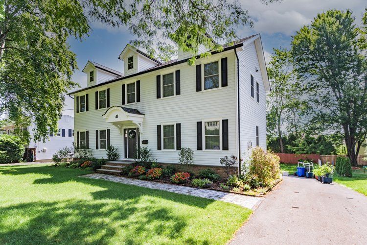 White house with black shutters, green lawn, trees, and a driveway.