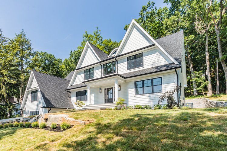 White two-story house with black trim, surrounded by trees on a sunny day.
