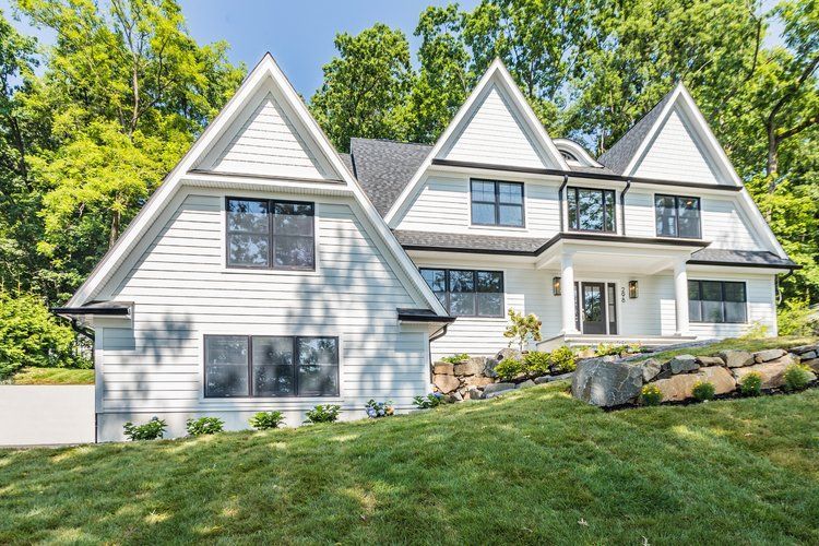 White two-story house with black trim, multiple peaked gables, and lush green lawn.