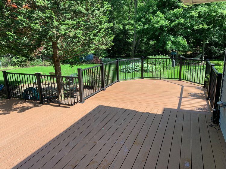 A composite deck with black railing overlooks a backyard with a small tree.