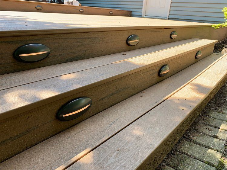 Deck steps with built-in lights. Brown composite decking with dark oval lights set into each step.
