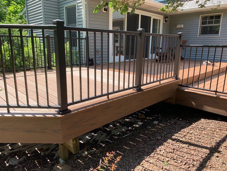 Brown composite deck with black metal railing, next to a gray house, sunny day.
