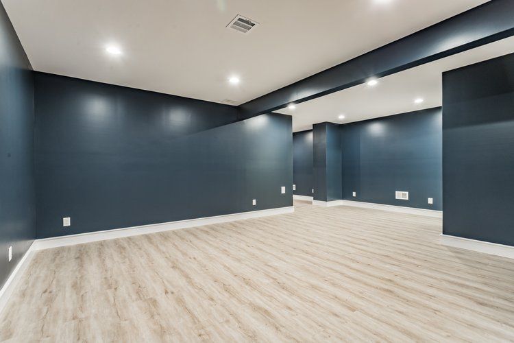 Empty basement room with light wood floors and dark blue walls; recessed lighting.