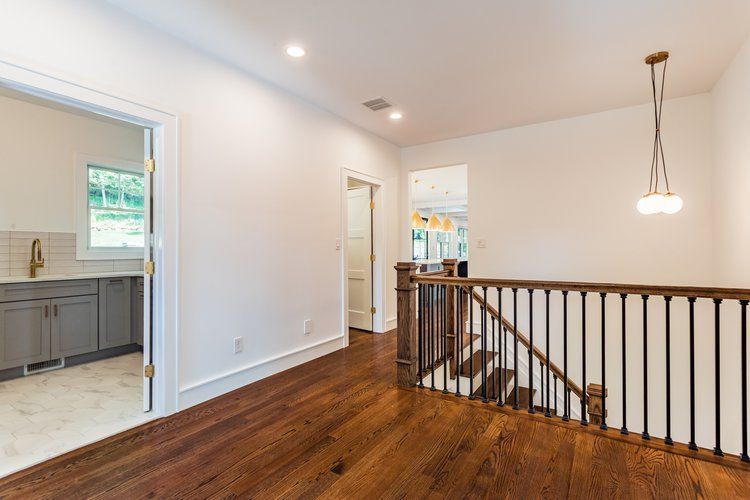 Hallway with hardwood floor, stairs, and a doorway to a gray-cabineted room.