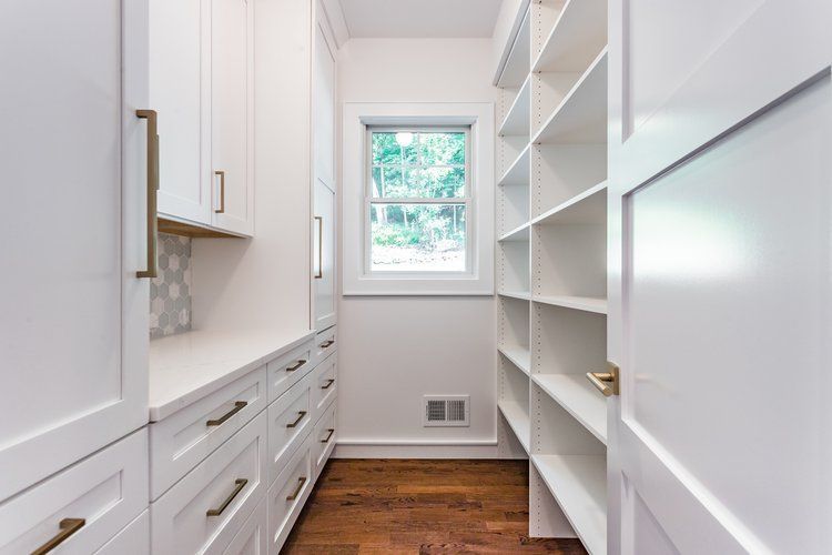 White pantry with cabinets, drawers, open shelves, and window; wood floor.