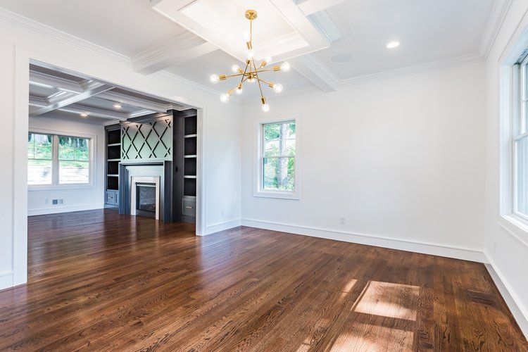 Empty room with dark wood floors, white walls, and a view into a room with fireplace and bookshelves.