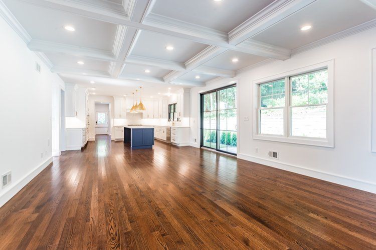Spacious room with dark wood floors, white coffered ceiling, and an open kitchen.