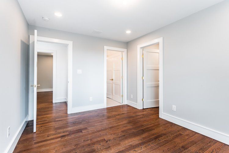 Empty room with wood floor, gray walls, white trim, and three white doors.