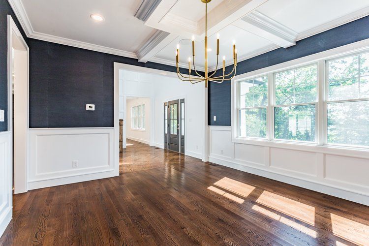 Formal dining room with dark blue walls, white trim, hardwood floors, and gold chandelier.