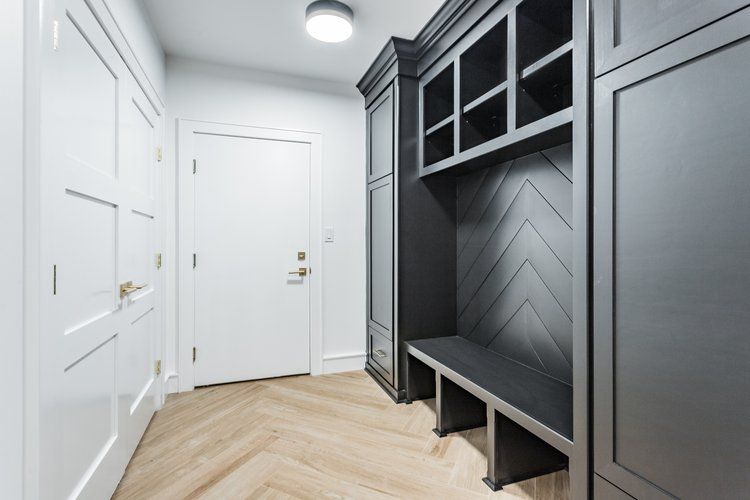 Entryway with dark gray built-in storage unit, white door, and herringbone wood floor.