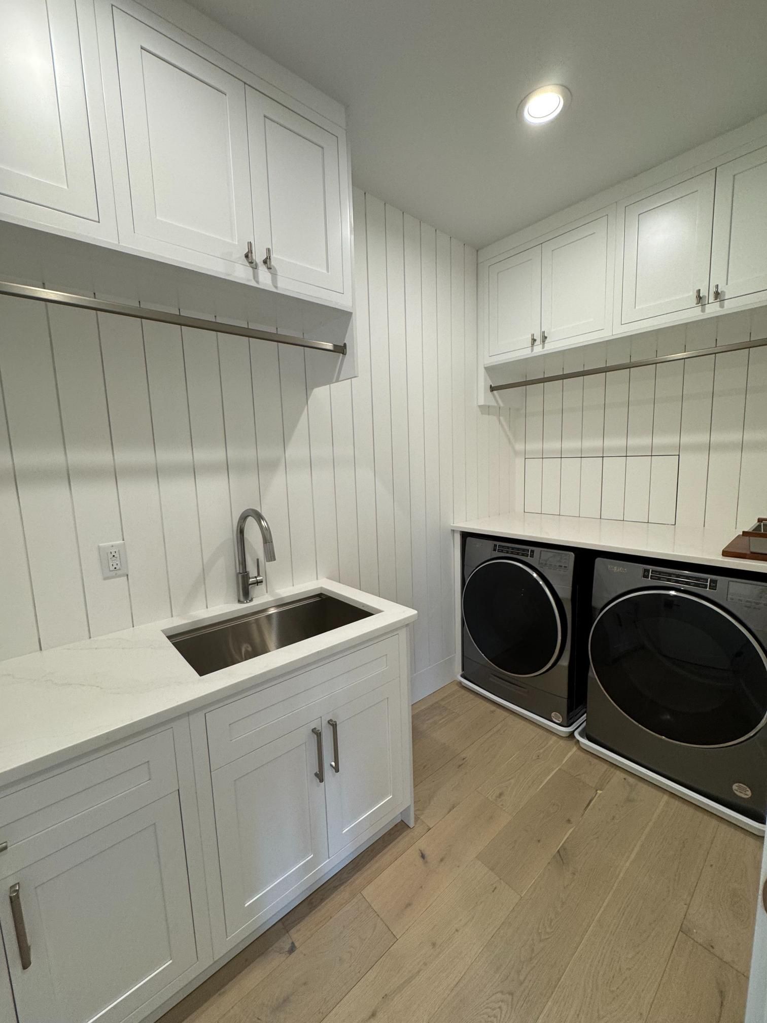 White laundry room with cabinets, sink, washer/dryer, and wood floors.