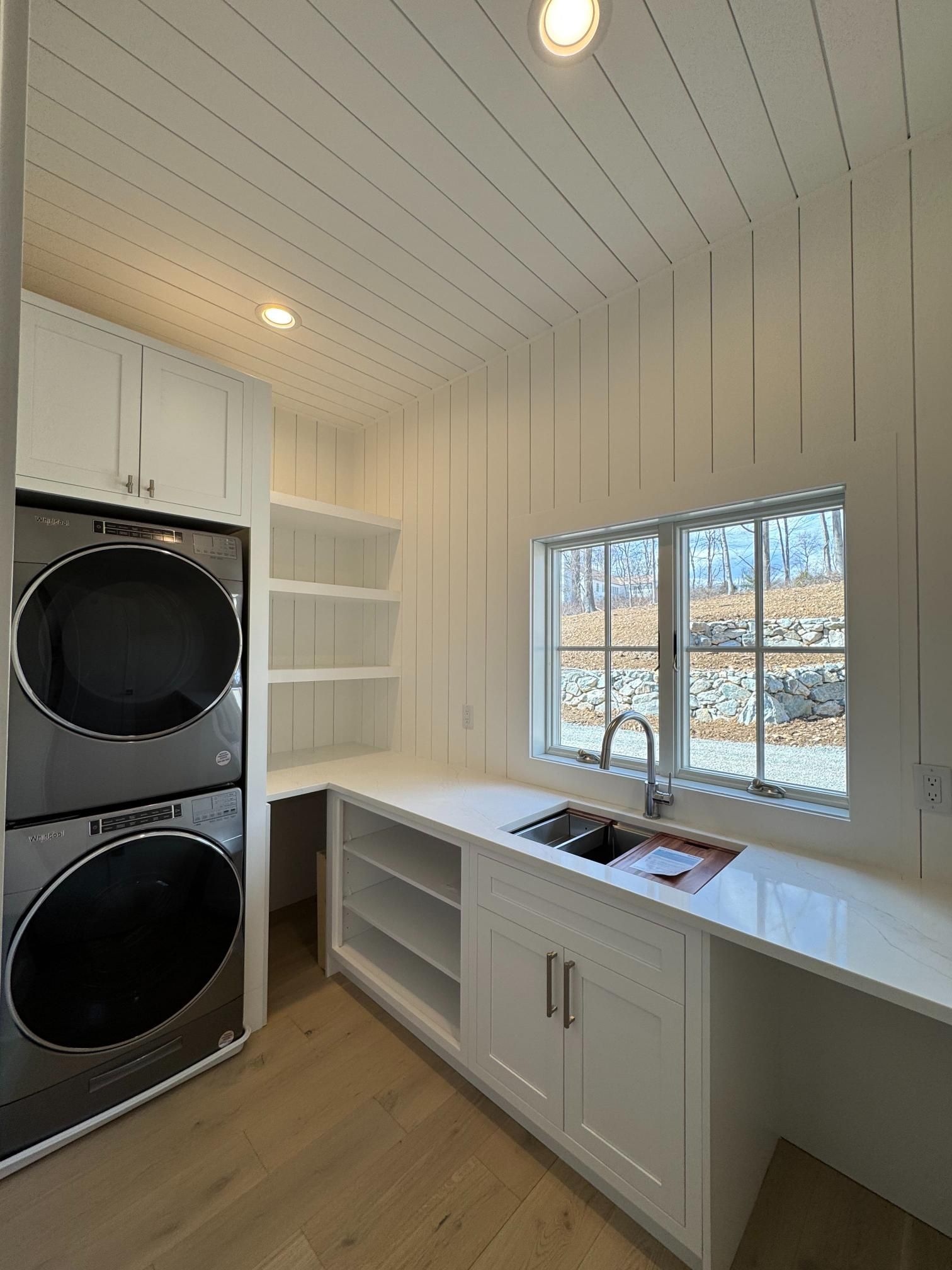 Laundry room with stacked silver washer/dryer, white cabinets, sink, and window.