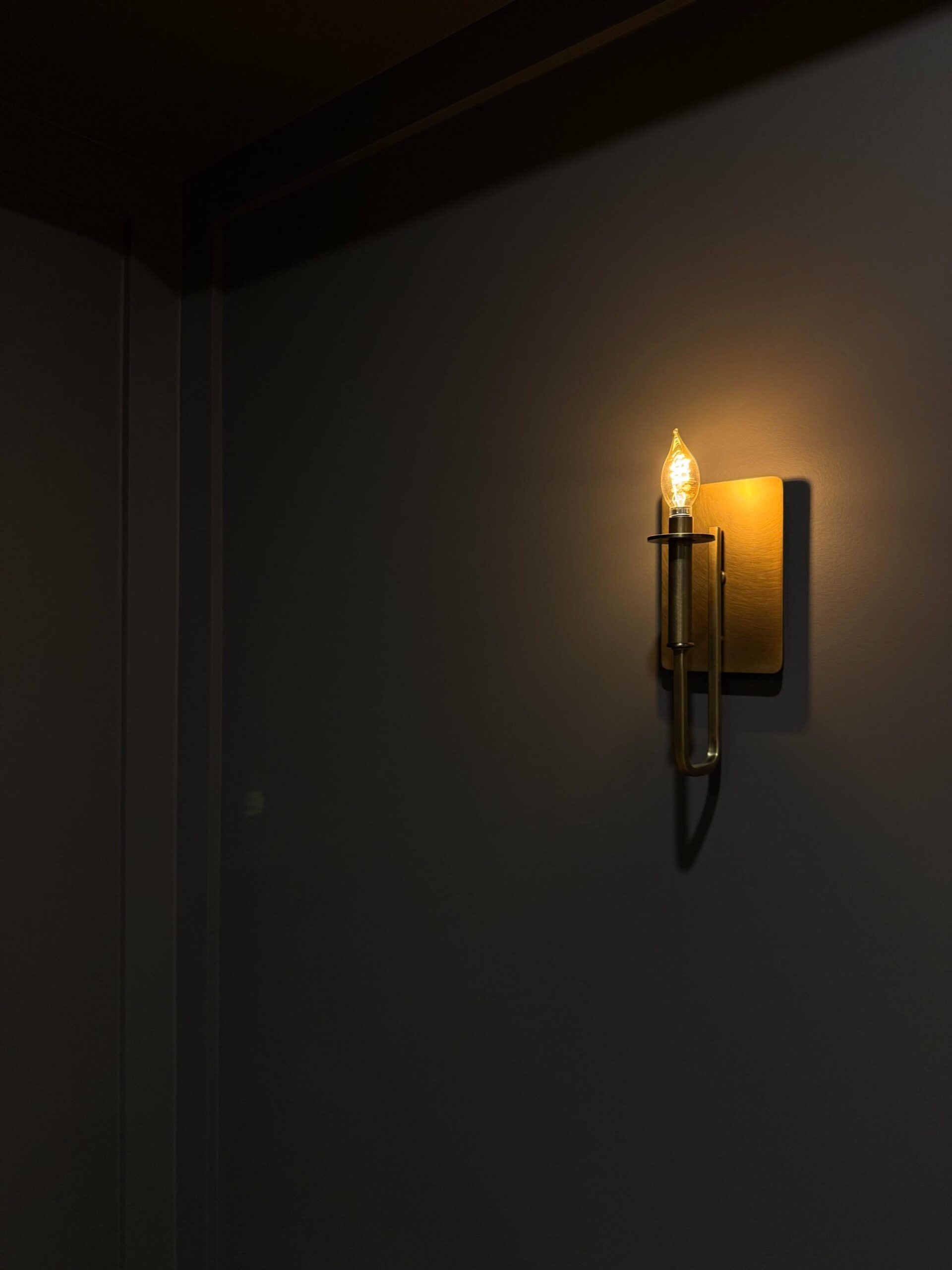 A single sconce with a lit bulb on a dark gray wall, in a corner.
