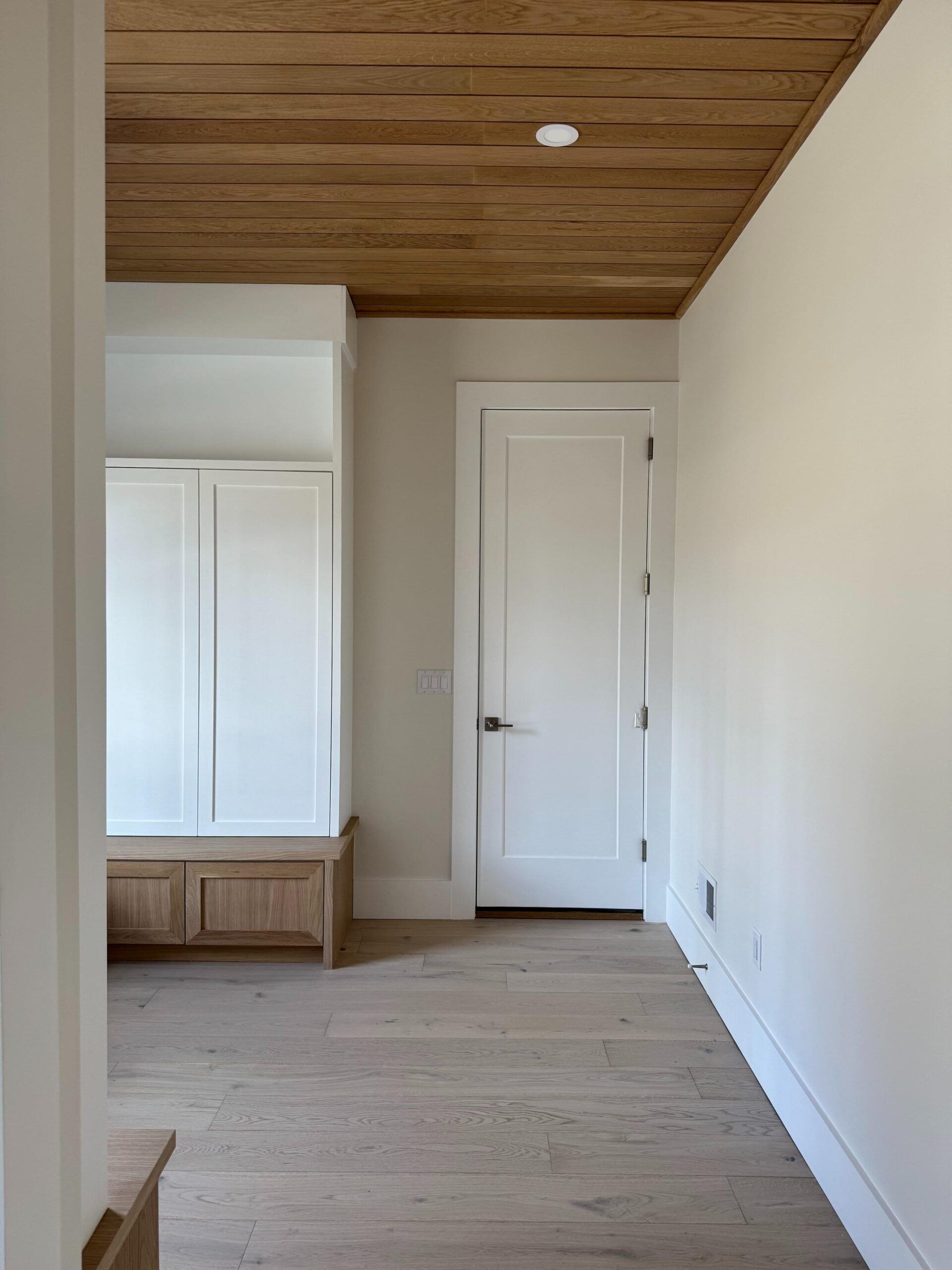 Hallway with wood ceiling, white walls, built-in storage, light wood floor, and a closed white door.