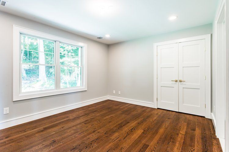 Empty room with hardwood floors, a large window, and double doors; light gray walls, white trim.