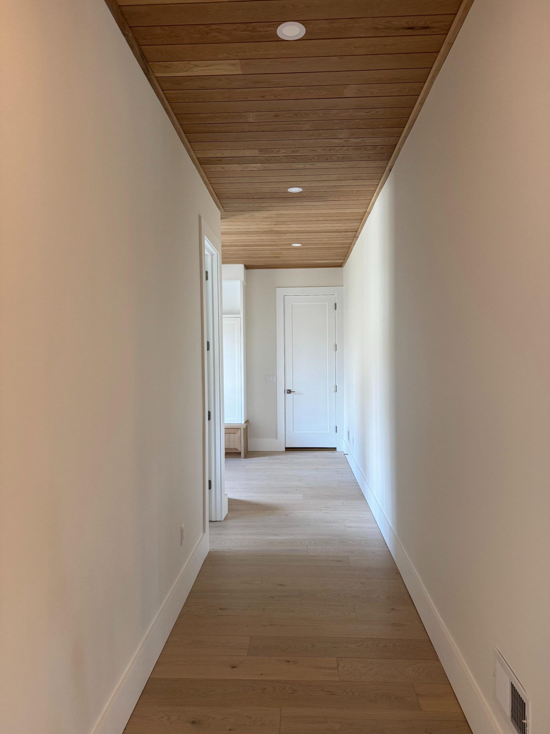 Narrow hallway with wood ceiling, white walls, and a door at the end.