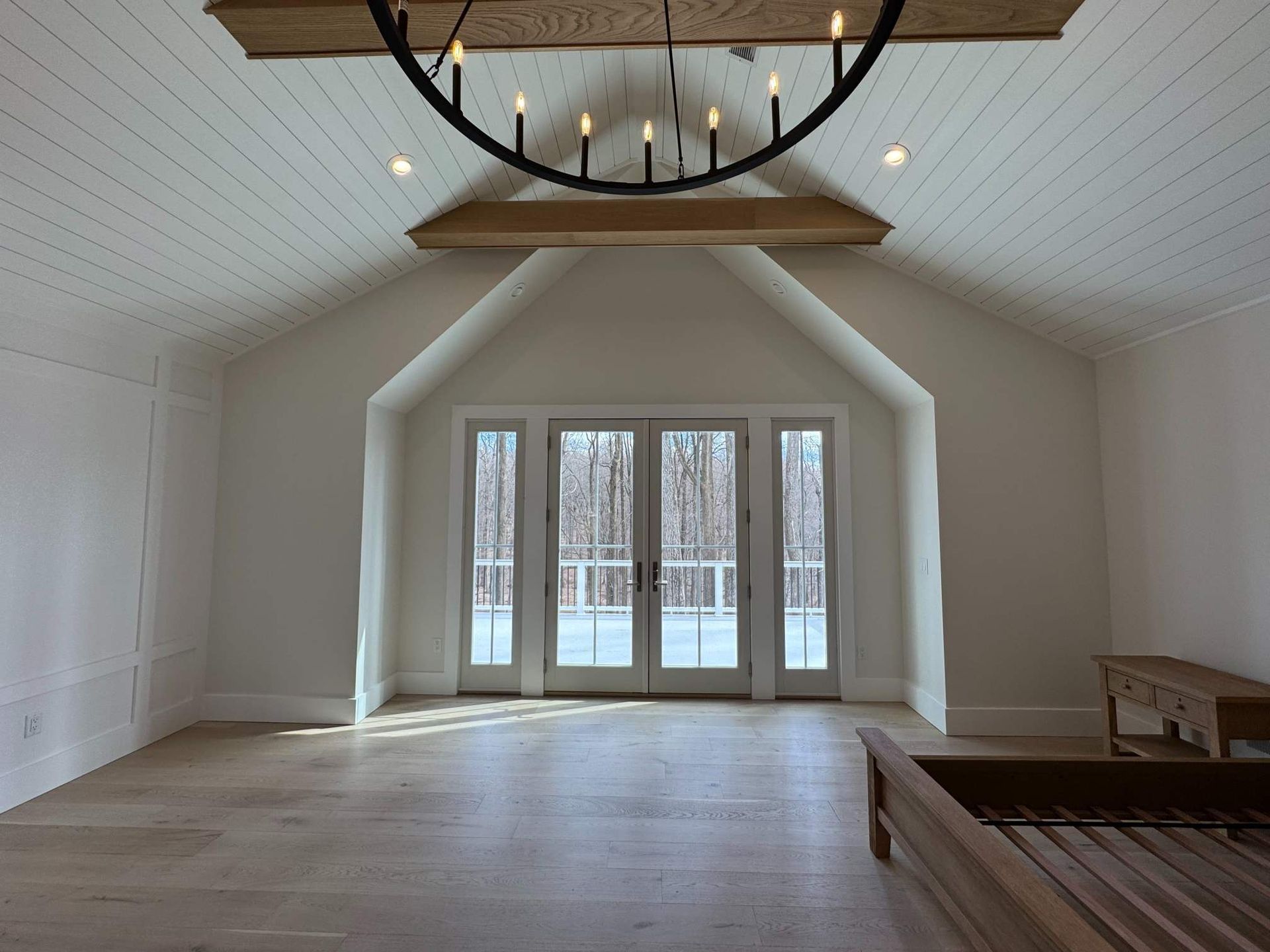 Empty room with wood floors, white walls, and a large window looking out onto trees.
