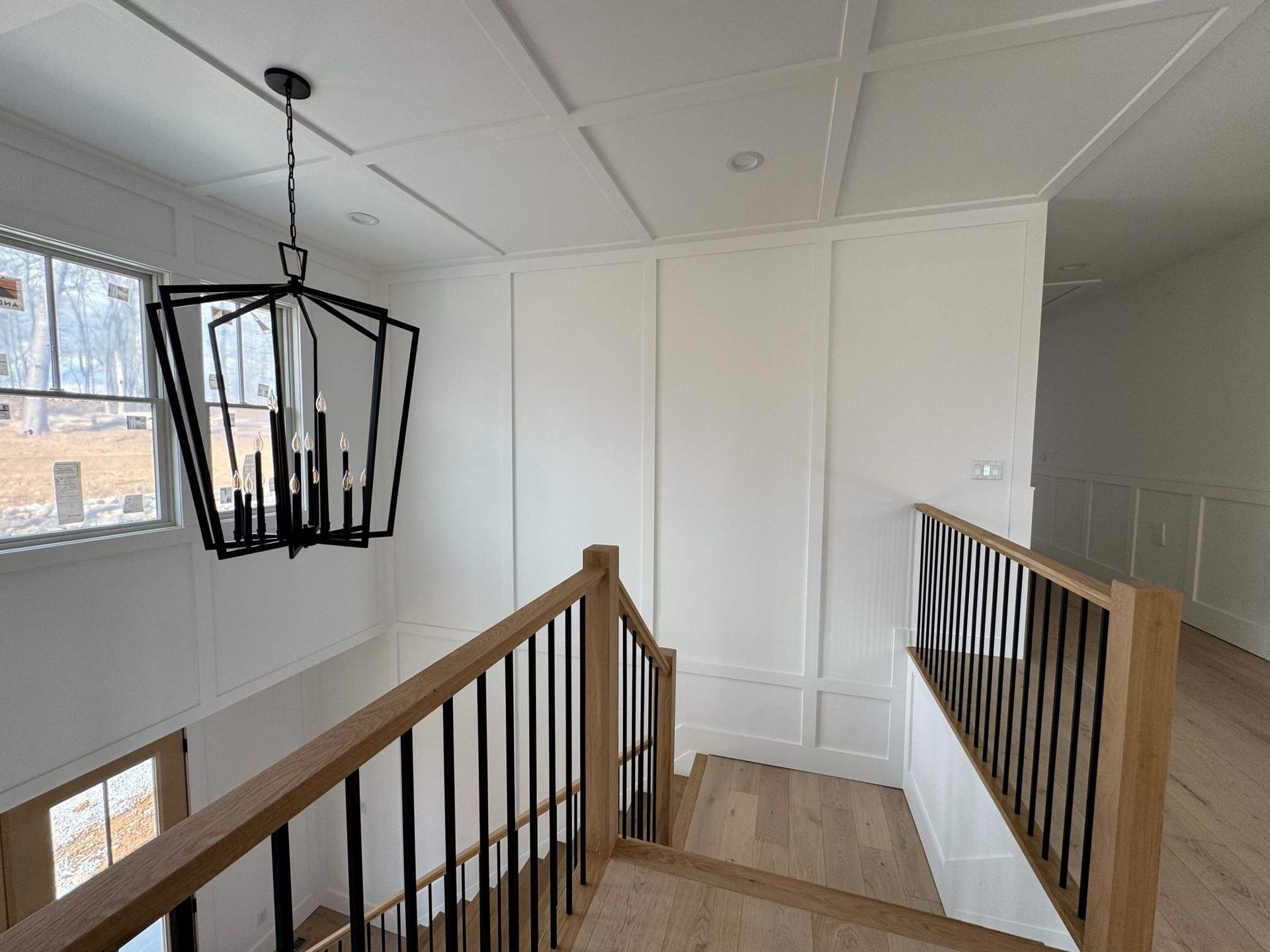 A modern entryway with a chandelier, staircase, and white paneling.