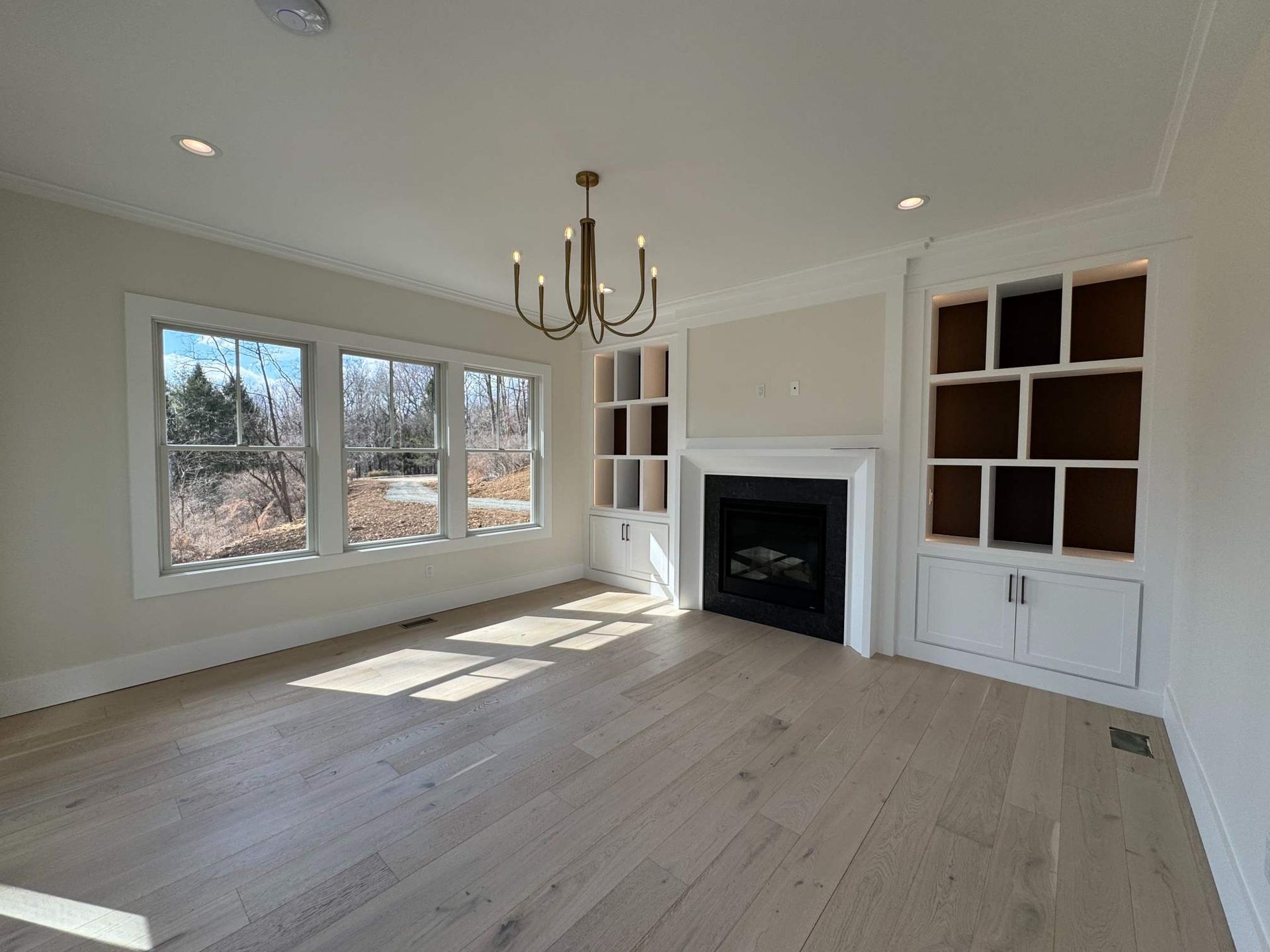 Spacious room with fireplace, built-ins, chandelier, and large windows overlooking nature.