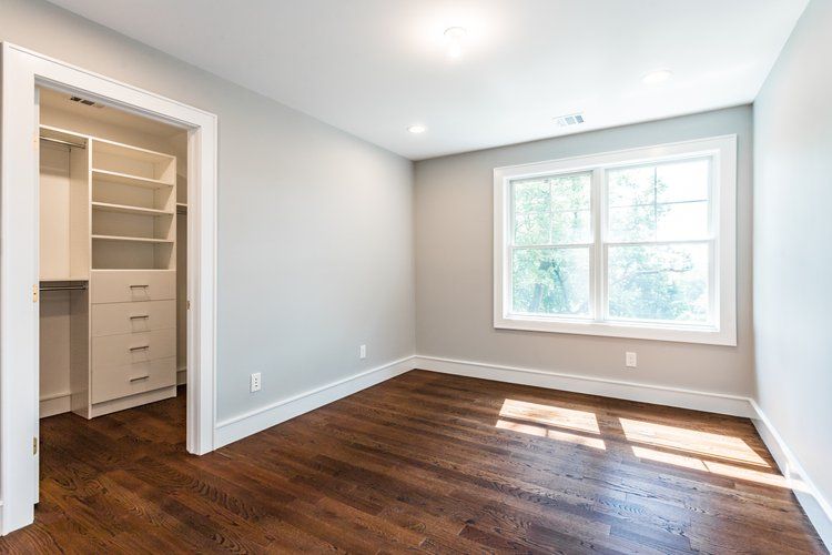 Empty bedroom with hardwood floor, gray walls, walk-in closet, and a bright window.