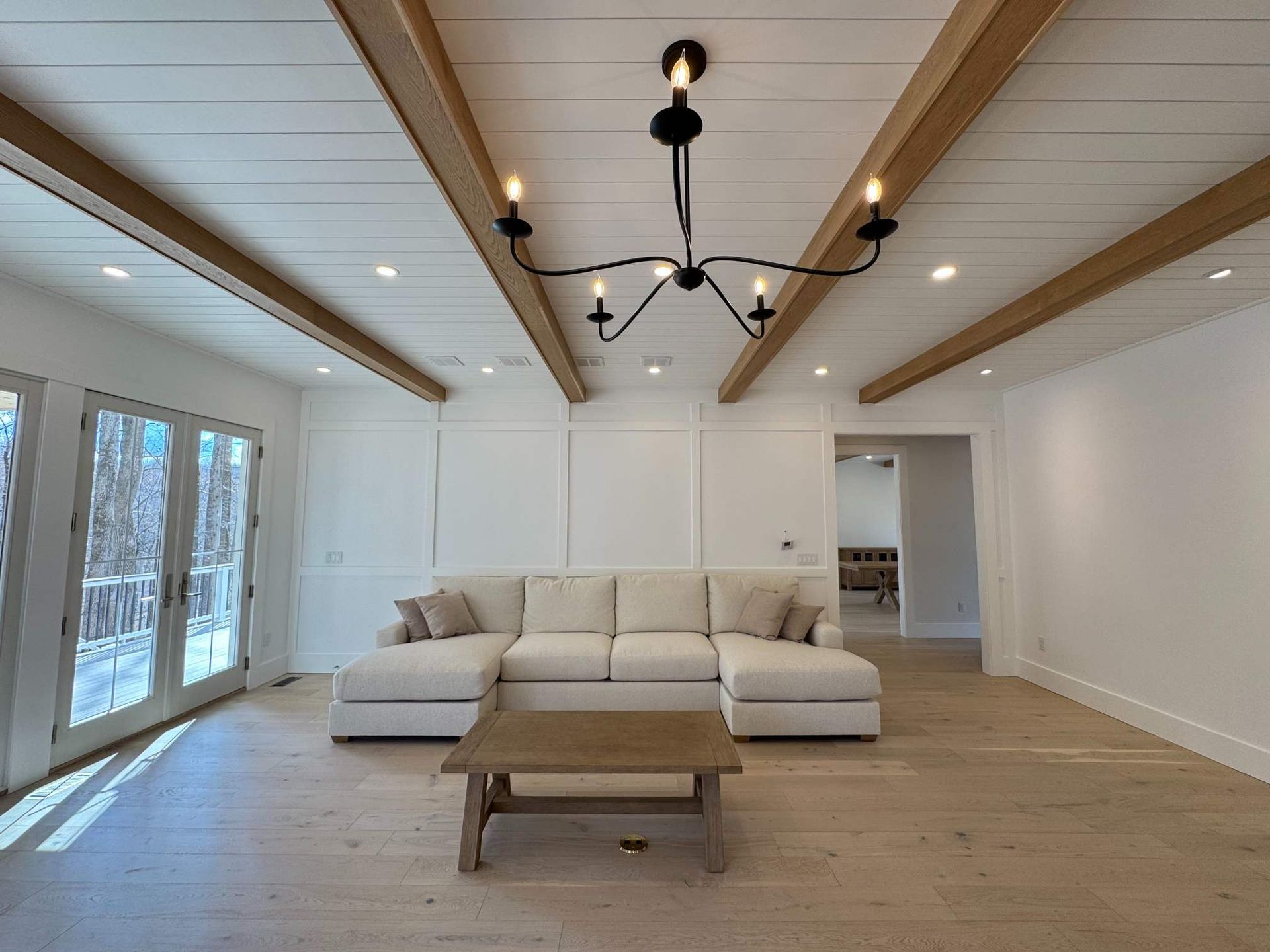 Spacious living room with white walls, a beige sectional sofa, and wood beams.