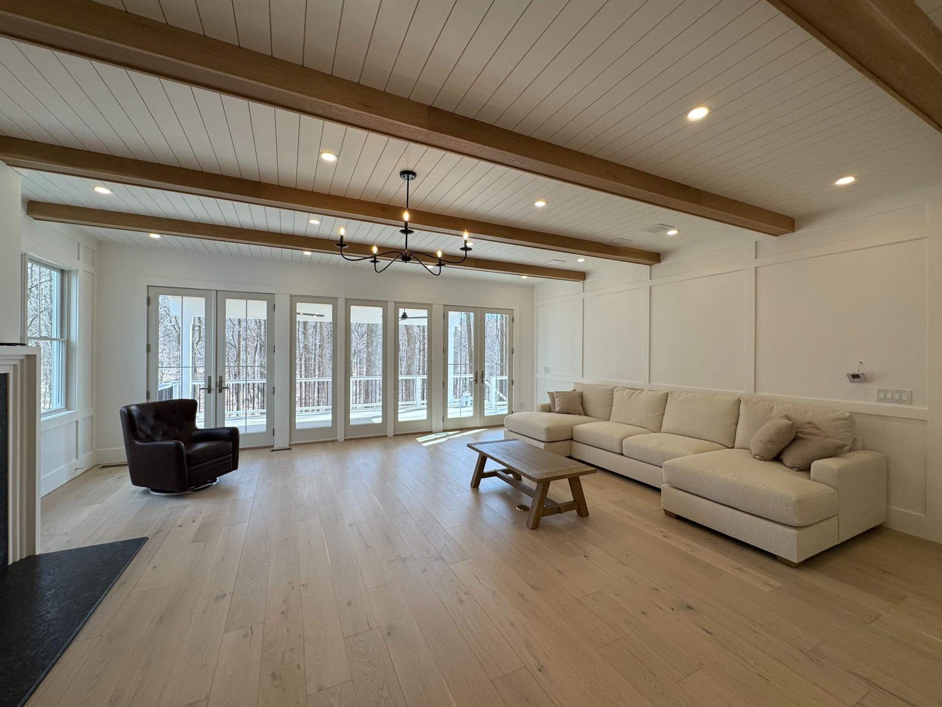 Spacious living room with white walls, light wood floors, and ceiling beams, French doors, and a large sectional.