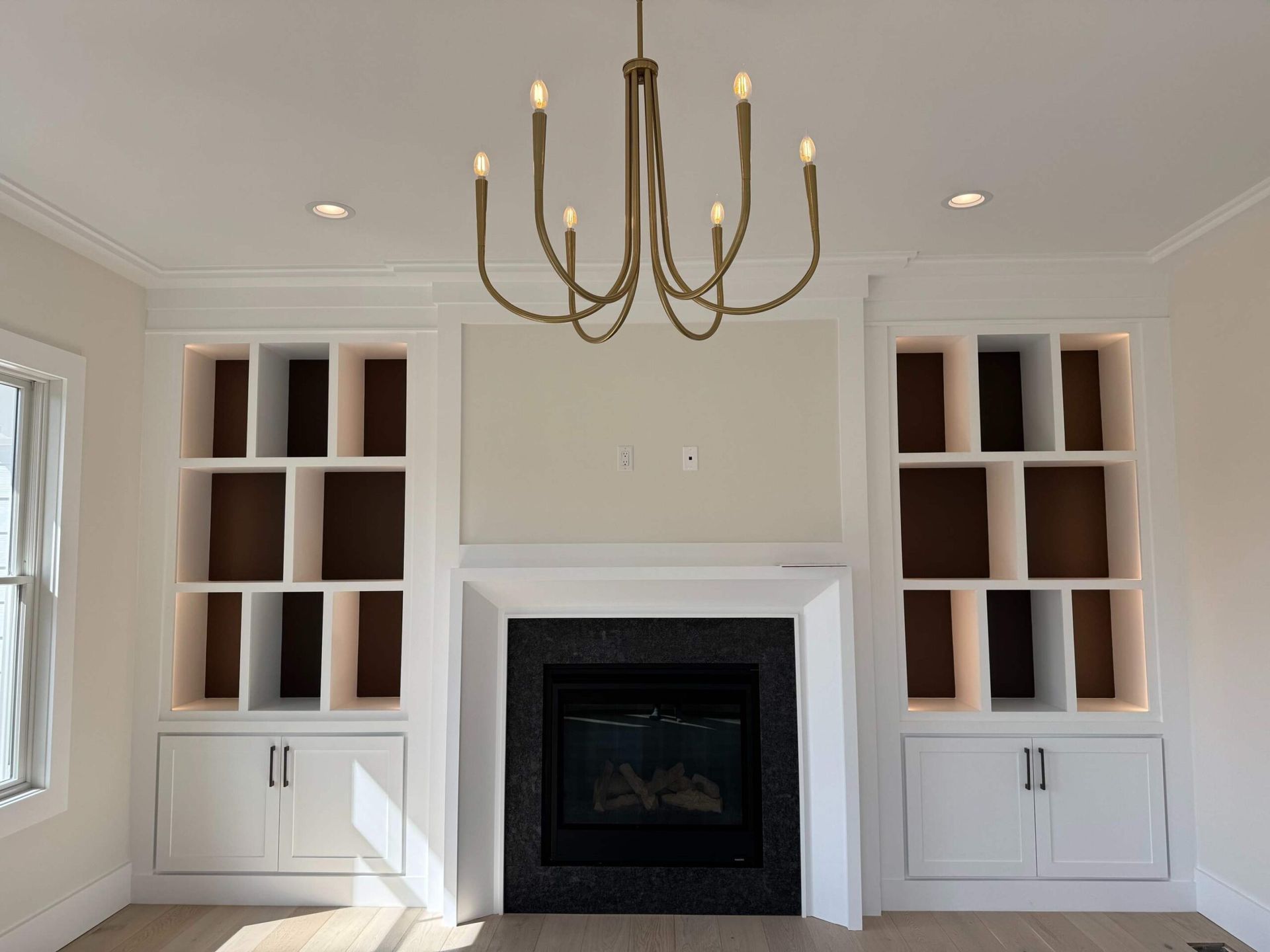 Living room with built-in bookshelves flanking a fireplace with a black tile surround; a gold chandelier hangs overhead.