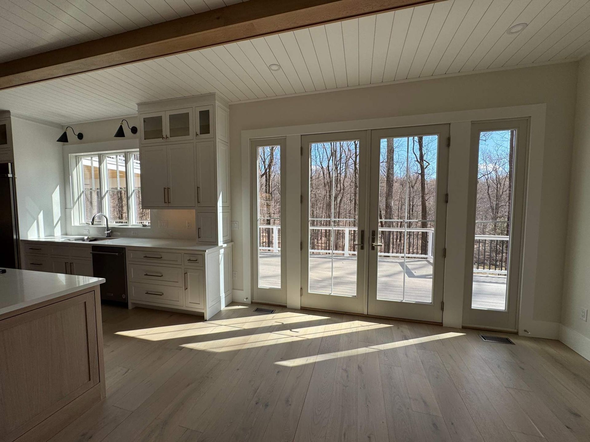 Kitchen with light wood floor and cabinets, a view to a deck through glass doors.