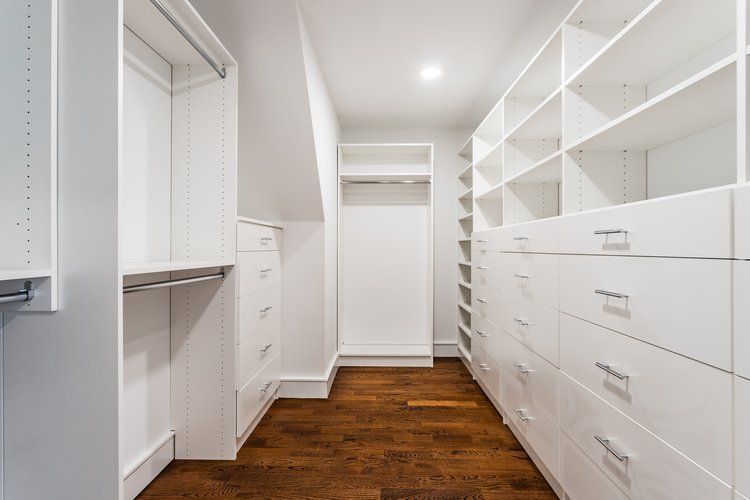 White closet with shelves, drawers, and hanging rods. Dark wood floor.