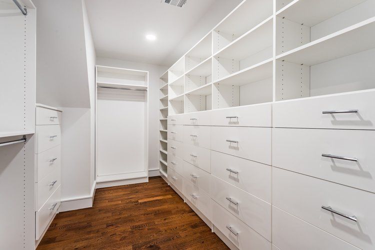 White walk-in closet with shelves and drawers, brown wood floor.