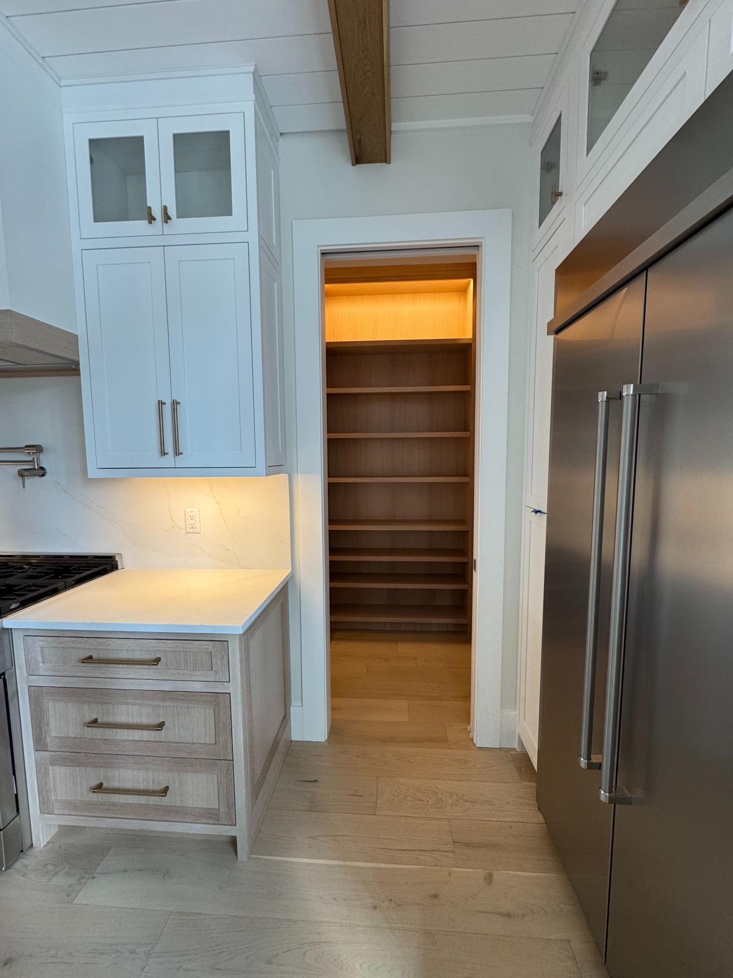 Kitchen with pantry doorway. Light wood shelves, white cabinets, and a stainless steel refrigerator.