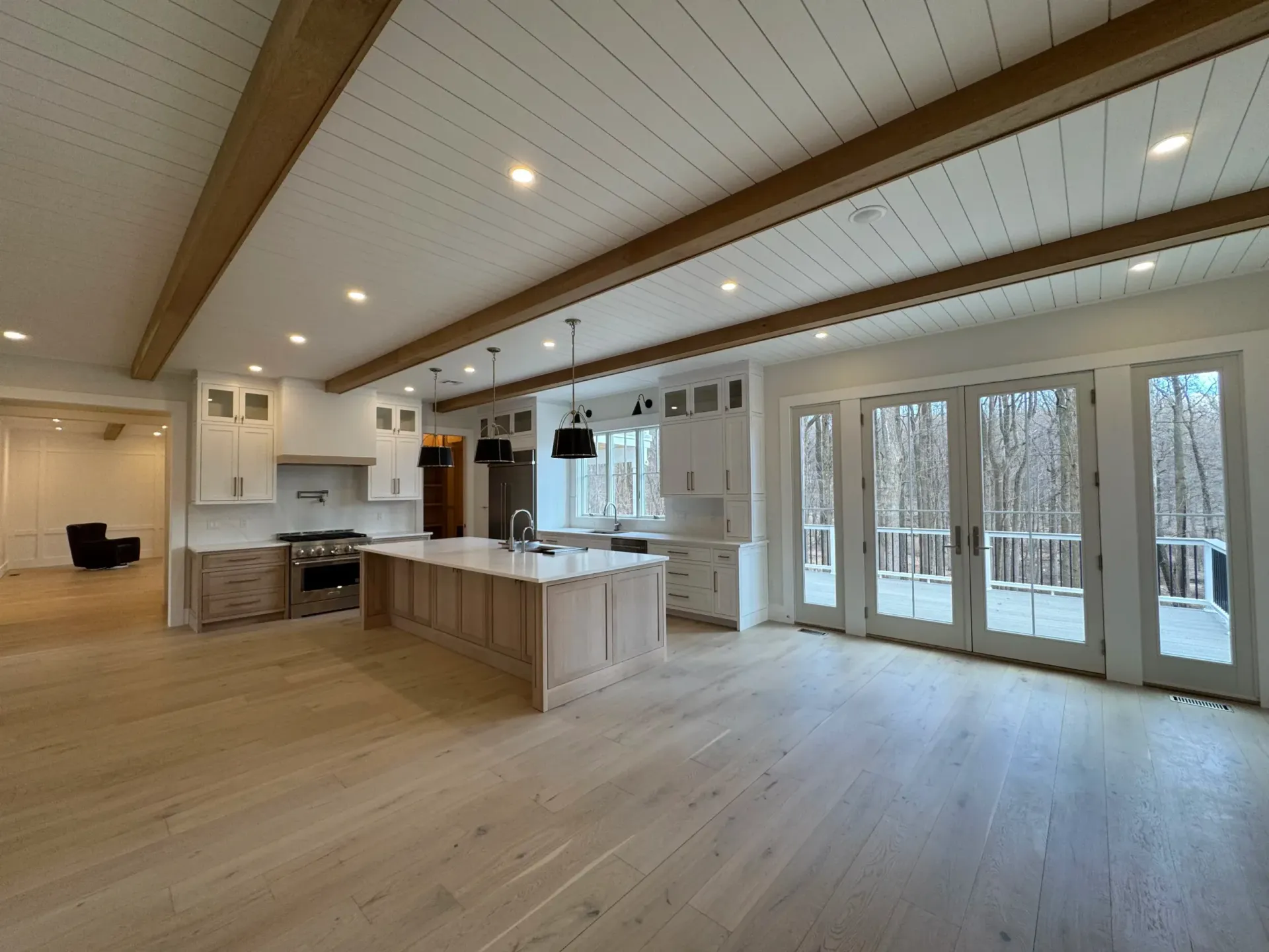 Spacious kitchen with wood beams, light wood floors and cabinets, white countertops and walls, and large windows.