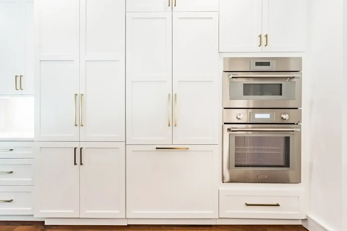White kitchen cabinets with built-in stainless steel microwave and oven; gold handles.