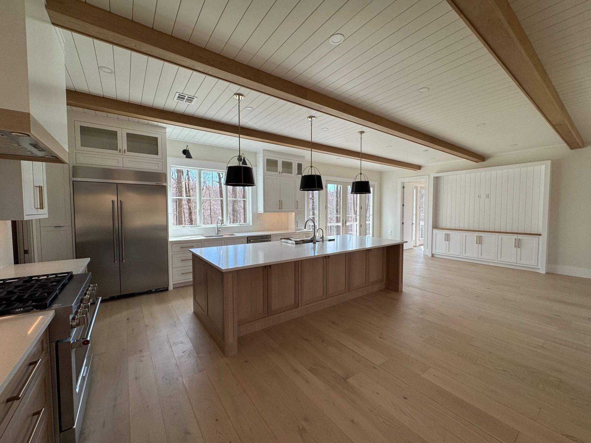 Modern kitchen with light wood floors, white cabinets, and a large island with three black pendant lights.