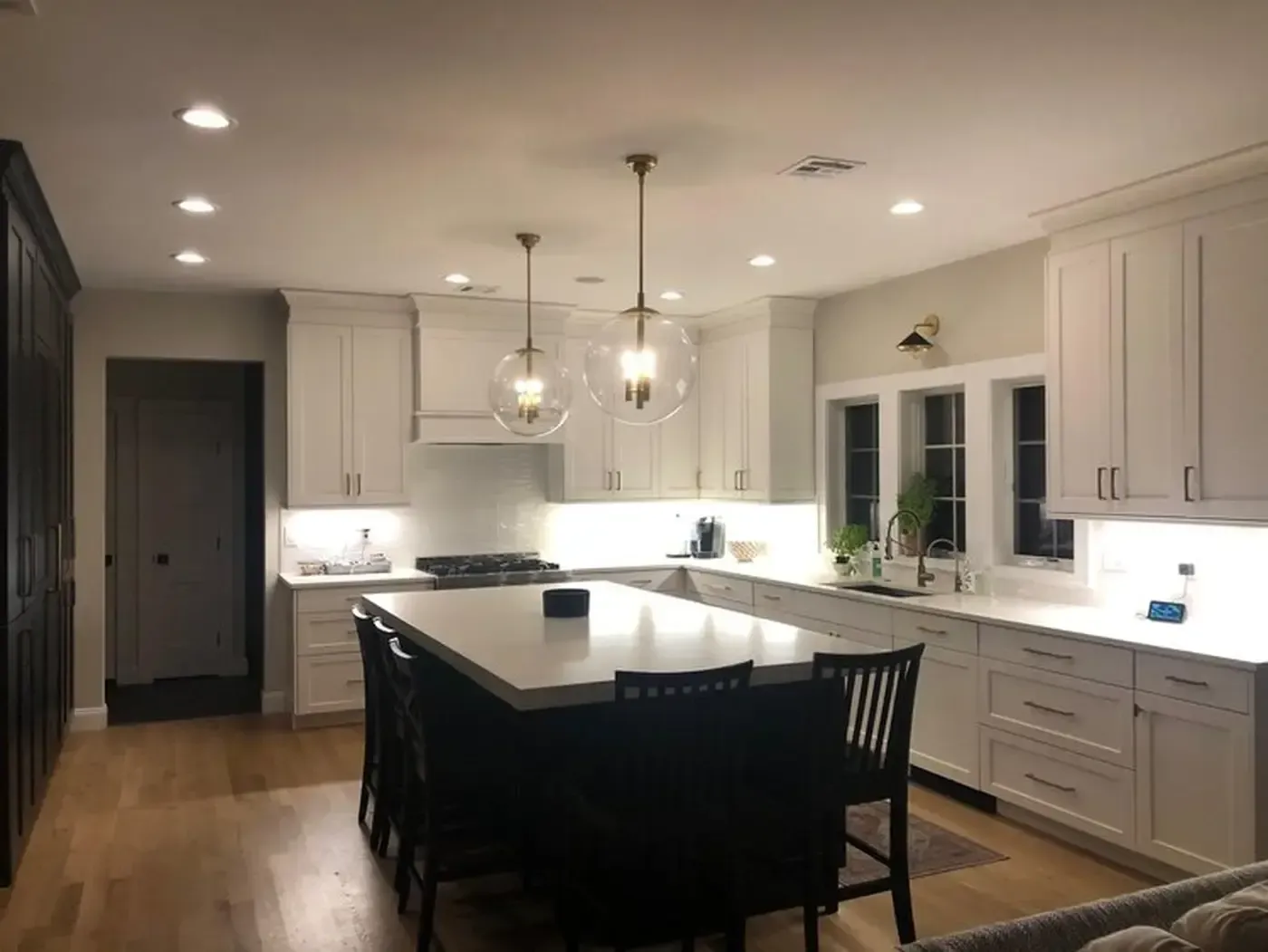 Brightly lit kitchen with white cabinets, dark island, and glass pendant lights.