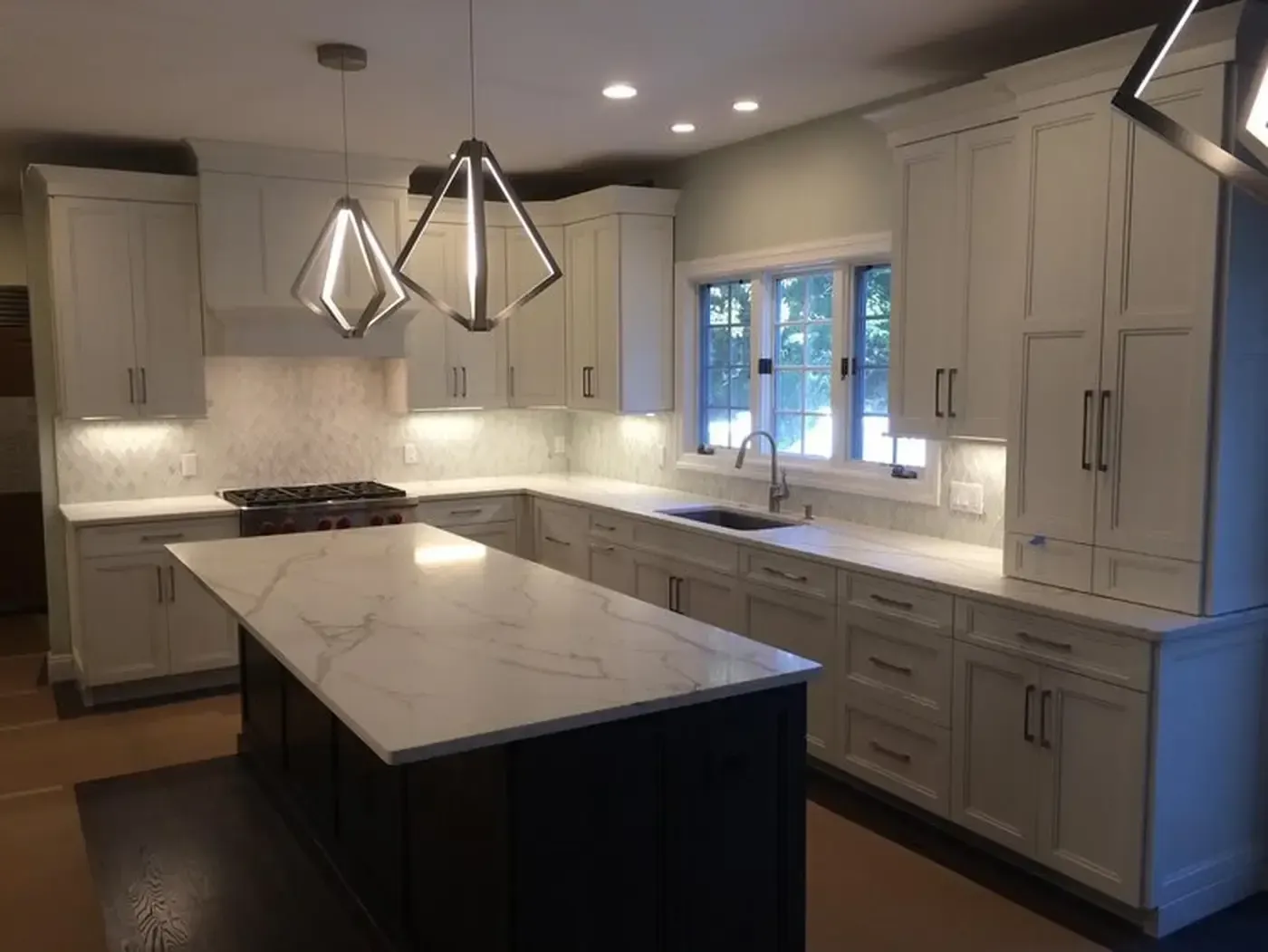 Modern kitchen with white cabinets, dark island, and geometric pendant lights.