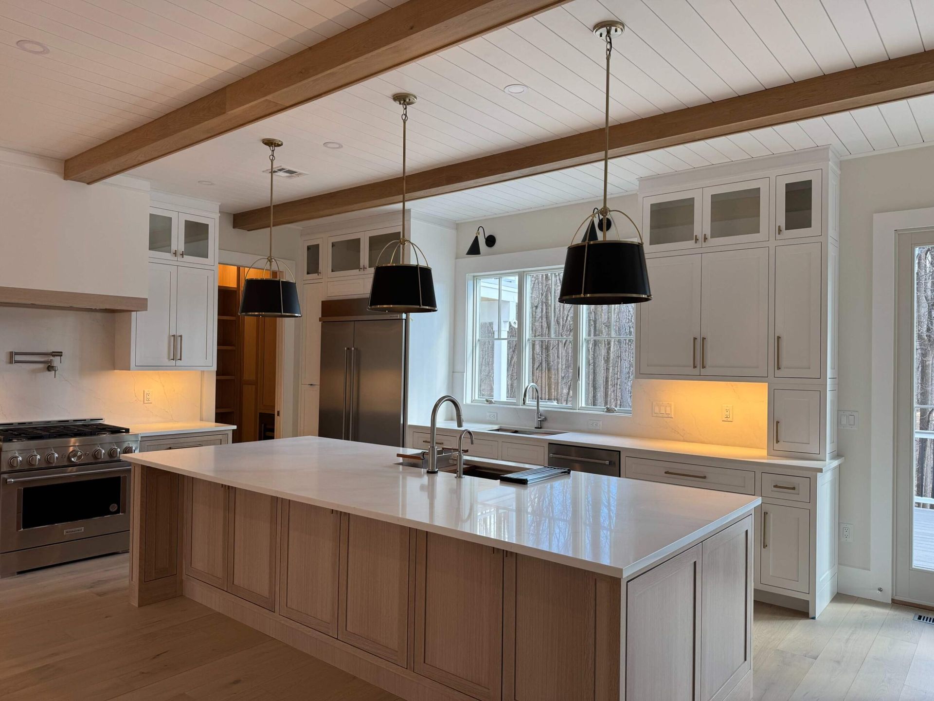 Bright kitchen with island, white and light wood cabinets, stainless steel appliances, and black pendant lights.