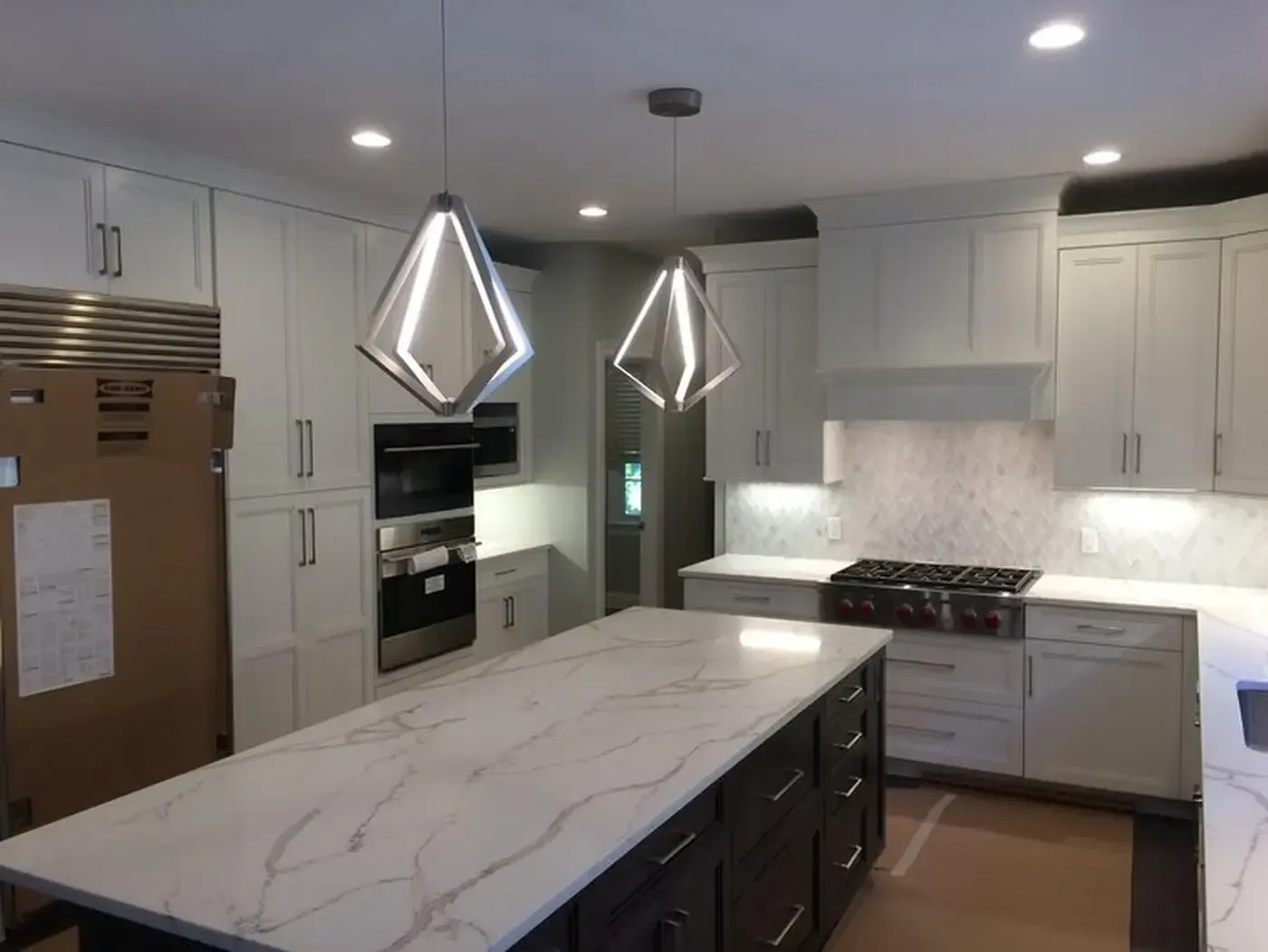 Modern kitchen with a white marble island and cabinets, stainless steel appliances, and two geometric pendant lights.