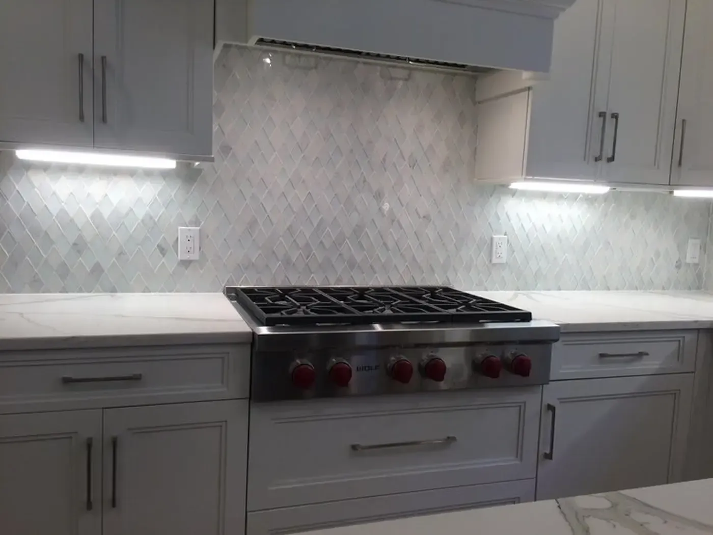 White kitchen with stove, cabinets, and diamond-patterned backsplash, under cabinet lighting.