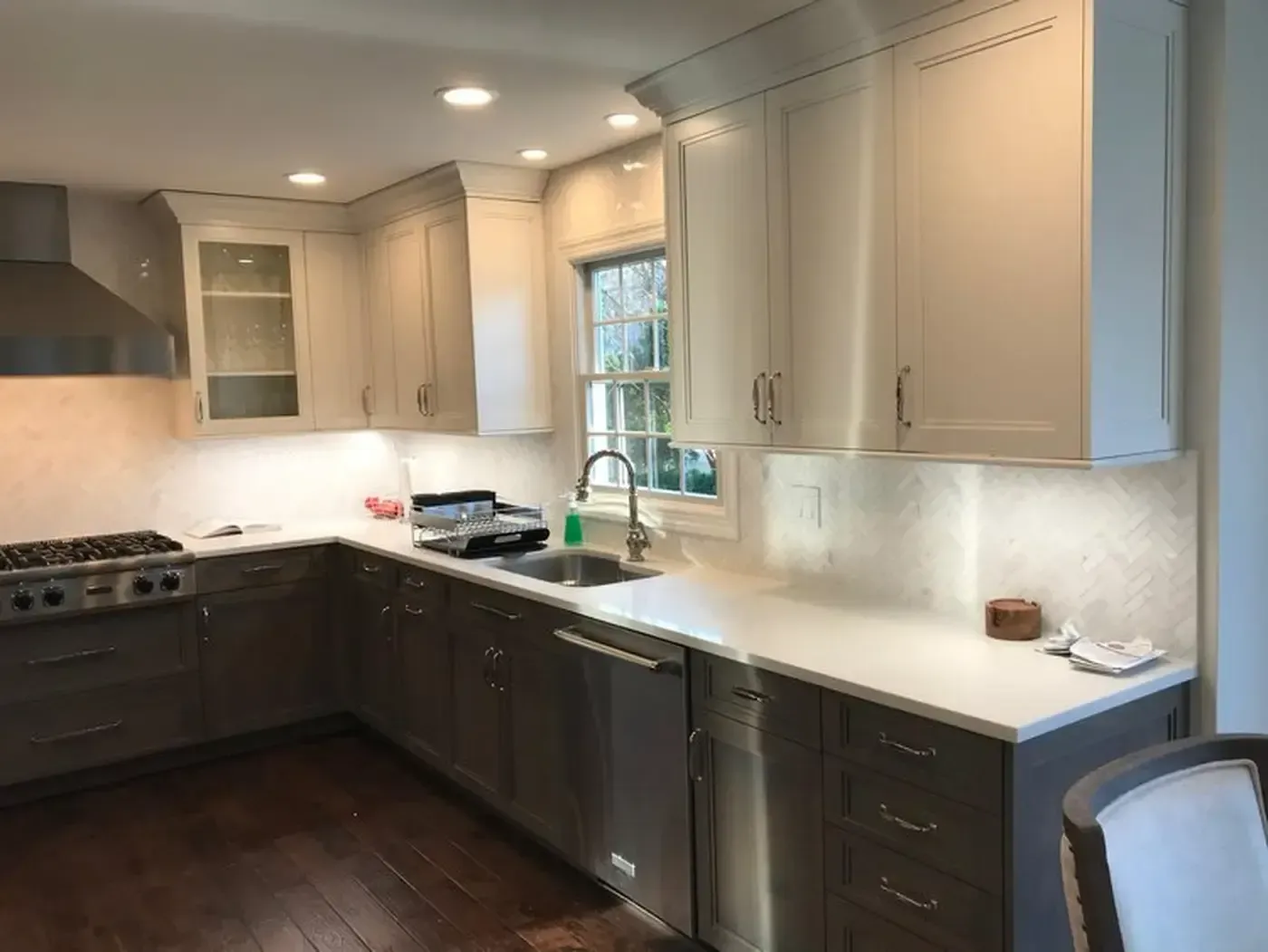 L-shaped kitchen with white countertops and light-colored cabinets. Stainless steel appliances and dark wood flooring.